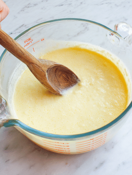 Blueberry yogurt muffin batter being mixed in a glass measuring bowl with a wooden spoon, ready for baking.