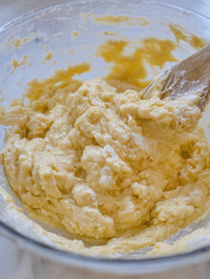 Rough, thick blueberry yogurt muffin dough being mixed with a wooden spoon in a glass bowl.