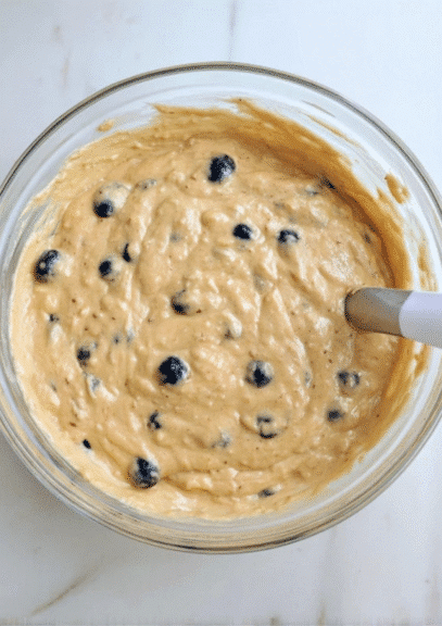 Blueberry muffin batter in glass mixing bowl with visible blueberries