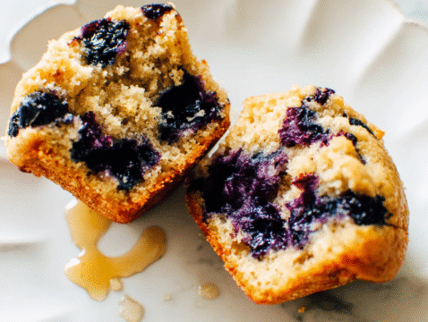 Close-up of a healthy blueberry muffin split in half, showing a moist crumb and bursting blueberries.