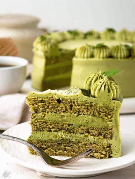 Slice of matcha cake recipe with green tea frosting and mint on a white plate